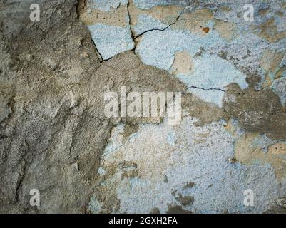 Verwitterte und rissige Betonwand mit blauem Kalk und verschiedenen Mörtelmischungen im Laufe der Zeit erhalten. Abblätternder Putz von der Oberfläche der Zementstruktur. Stockfoto