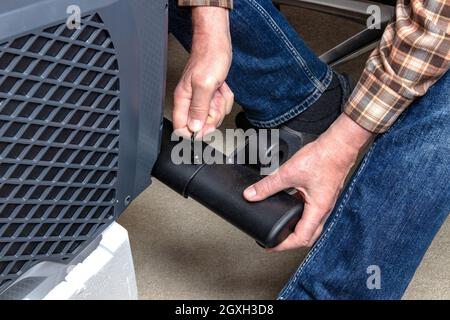 Montage eines modernen Fitnessgeräts. Schrauben Sie die Vorderfüße mit Rollen auf einem Crosstrainer von einem Handwerker an. Fitnessgeräte für Körpertraining. Stockfoto