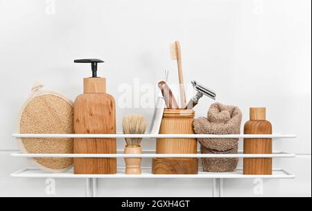 Nahaufnahme von natürlichen Holzflaschen mit kosmetischen Kosmetikpflegeprodukten, Handtüchern, Hygiene-, Pflege- und Rasierzubehör auf dem Badregal über weißem Backgroun Stockfoto