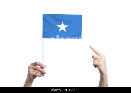 Eine schöne weibliche Hand hält eine Somalia-Flagge, auf der sie den Finger ihrer anderen Hand zeigt, isoliert auf weißem Hintergrund. Stockfoto