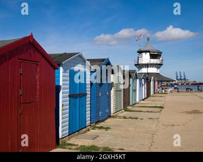 Eine Reihe farbenfroher Strandhütten mit Harwich Low Lighthouse, Maritime Museum und Felixstowe Container Port Distance, Harwich, Essex, England, Großbritannien Stockfoto