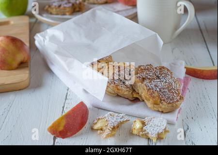 Apfelpfannkuchen für unterwegs. Frische und hausgemachte Pfannkuchen in der Pfanne mit Vollkornmehl und frischen Äpfeln. Serviert in einer Papiertüte. Stockfoto