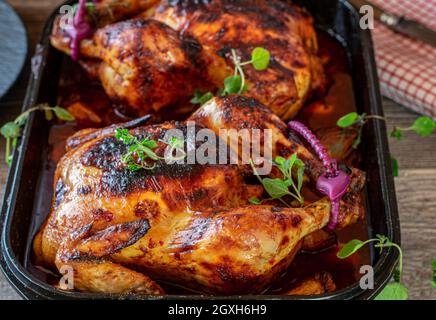 Ganzes Huhn in einem leckeren würzigen Honig, Knoblauchsauce auf rustikalem Tischhintergrund in einer Backform Stockfoto