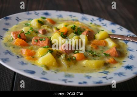 Teller mit frisch gekochter Kartoffelsuppe und Wurst. Serviert auf einem Holztisch mit Löffel. Nahaufnahme und abgelegene Sicht Stockfoto