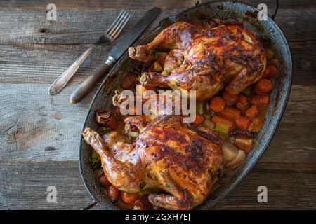 Hähnchen mit Wurzelgemüse in einer rustikalen Kasserolle rösten. Hausgemachte Mahlzeit isoliert auf rustikalen und Holztisch von oben Stockfoto