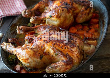 Hähnchen mit Wurzelgemüse in einer rustikalen Kasserolle rösten. Hausgemachte Mahlzeit isoliert auf rustikalen und Holztisch von oben Stockfoto