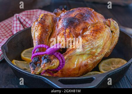 Im Ofen gegrilltes Hähnchen in einer gusseisernen Pfanne auf einem Holztisch. Isoliert und Vorderansicht Stockfoto