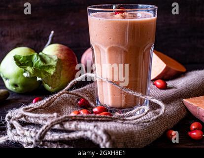 Gesunder Obst-, Gemüse-Smoothie mit Wildfrüchten wie wilden Äpfeln und Hagebutten, gemischt mit Süßkartoffeln und in einem Glas auf einem Holztisch serviert Stockfoto