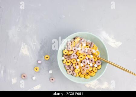 Mehrfarbige Müslischlaufen und Milch in einer Schleife, goldener Löffel auf grauem Hintergrund. Draufsicht, Kopierbereich. Frühstückskonzept Stockfoto