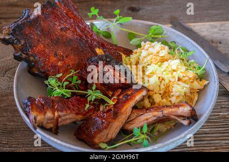 Im Ofen gebackene Spareribs, mariniert mit Barbecue-Sauce und Honig, serviert mit frischem, hausgemachtem Krautsalat, isoliert auf einem Holztisch Stockfoto