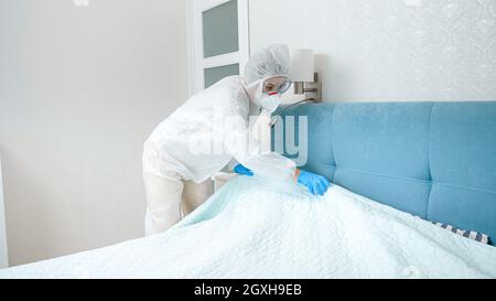 Hotelmädchen in schützendem medizinischen Anzug und Handschuhen, die das Hotelzimmer aufräumen. Desinfektion und Hygiene während der Covid-19- und Coronavirus-Pandemie. Stockfoto