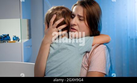 Porträt von jungen liebevollen Mutter beruhigend und streichelnd kleinen Jungen in Kinderzimmer in der Nacht verängstigt. Kind hat Angst und weint vor Albtraum oder Schlechtes Stockfoto