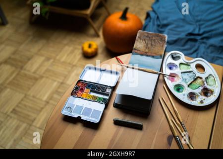 Aquarelle, Pinsel und Paletten auf dem Tisch neben einem Notizbuch mit Zeichnungen Stockfoto