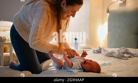 Kleines neugeborenes Baby weinend und schreiend, während Mutter Kleidung und Windeln auf dem Bett in der Nacht wechselt. Konzept der Babyhygiene, liebevolle und fürsorgliche Eltern Stockfoto