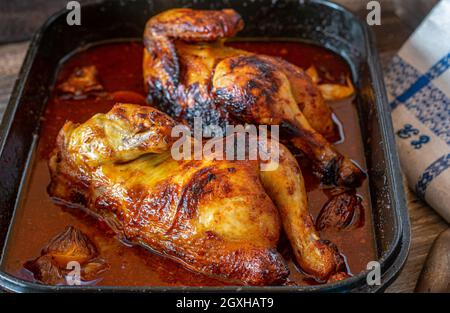 Würziges halbes Huhn in einem köstlichen Paprika, Knoblauch, Honigsauce serviert in einer Auflaufform auf einem Holztisch. Nahaufnahme und abgelegene Sicht Stockfoto