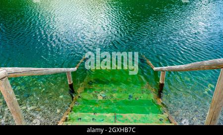 Wunderschönes ruhiges Wasser des Sees mit hölzernen Pier und Treppen, die ins Wasser führen. Transparentes Smaragdwasser Stockfoto