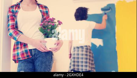 Glückliches Paar Haupterneuerungen zu tun, ist der Mann das Zimmer und die Frau halten den Topf mit Blumen Malerei. Stockfoto