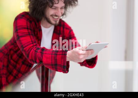 Junge Freiberufler in Bademantel mit Tablet-PC von zu Hause aus arbeiten Stockfoto