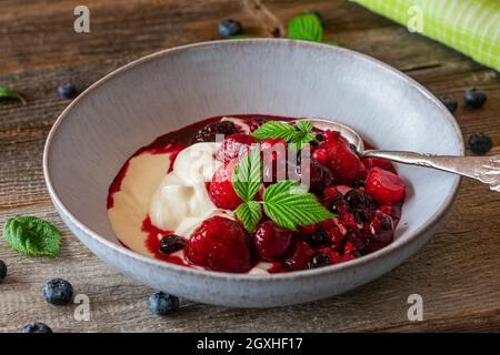 Hausgemachte gesunde Frühstückschüssel mit ikanischer Skyr und gemischten Beeren in einer Schüssel auf Holztisch serviert Stockfoto