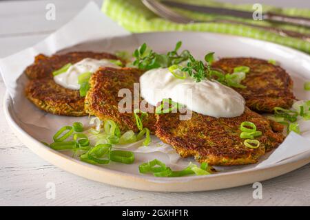 Gesundes glutenfreies Gericht mit Gemüsepfannkuchen, gebacken mit Karotten und Zucchini, serviert mit griechischem Joghurt-Dip und Kräutern auf einem weißen Teller. Stockfoto