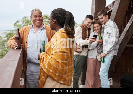 Verschiedene Gruppen junger Menschen trinken Bier auf dem Balkon während der Party am Lake House Stockfoto