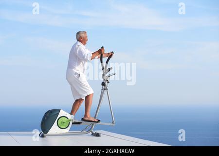 gesunde Senioren Mann arbeiten auf Fitness Laufband Maschine im modernen Haus Terrasse mit Meerblick Stockfoto