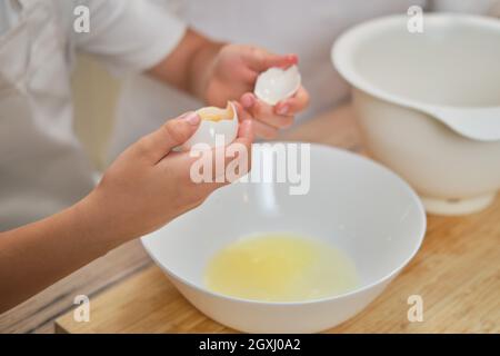 Junge Hände trennen das Eiweiß vom Eigelb für den Kuchen Stockfoto