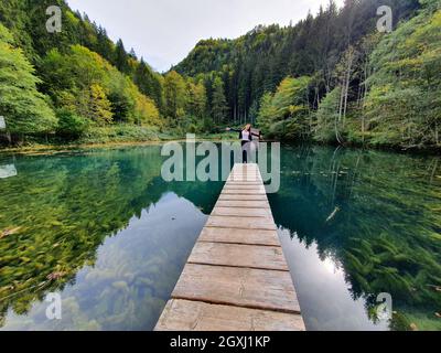 Schönes Mädchen auf einer hölzernen Landebahn mit Blick auf einen See bei Sonnenuntergang in Österreich Stockfoto