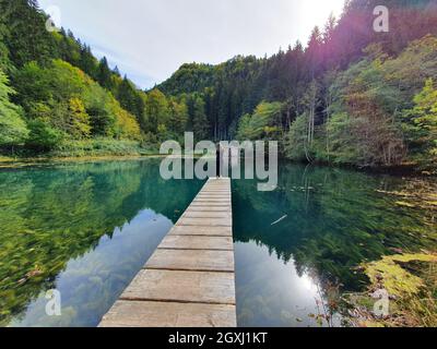 Schönes Mädchen auf einer hölzernen Landebahn mit Blick auf einen See bei Sonnenuntergang in Österreich Stockfoto