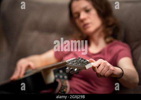 Frau, die Gitarre zu Hause auf der Couch stimmt. Stockfoto