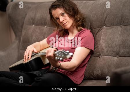 Frau, die Gitarre zu Hause auf der Couch stimmt. Stockfoto