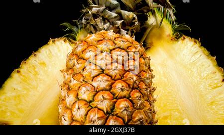 Abstraktes Foto von geschnittenen Hälften leckerer süßer Ananas auf schwarzem Hintergrund. Abstrakter Hintergrund exotischer Früchte. Stockfoto