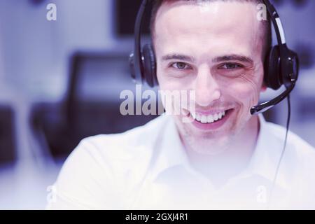 junge lächelnd männlichen Call Center-Betreiber macht seinen Job mit einem Kopfhörer Stockfoto