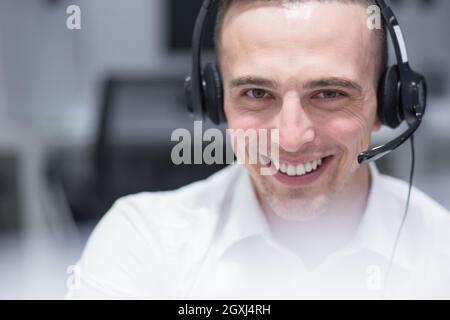 junge lächelnd männlichen Call Center-Betreiber macht seinen Job mit einem Kopfhörer Stockfoto