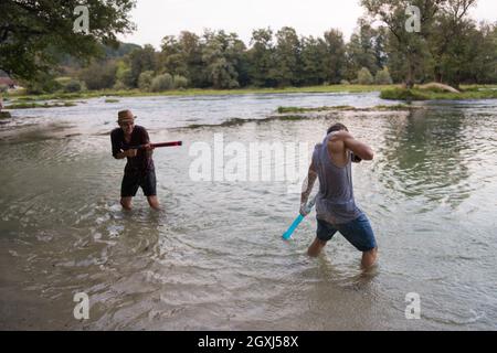 Junge Männer Spaß mit Wasserkanonen und Spritzwasser bei Sonnenuntergang auf dem Fluss Stockfoto