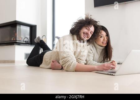 Junge schöne multiethnischen paar mit einem Laptop und Online-shopping zu Hause auf dem Boden Stockfoto