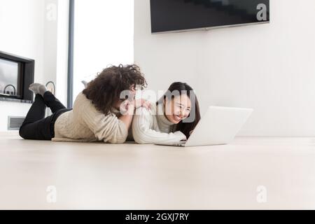 Junge schöne multiethnischen paar mit einem Laptop und Online-shopping zu Hause auf dem Boden Stockfoto