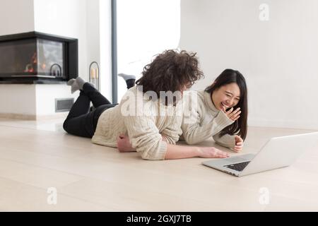 Junge schöne multiethnischen paar mit einem Laptop und Online-shopping zu Hause auf dem Boden Stockfoto