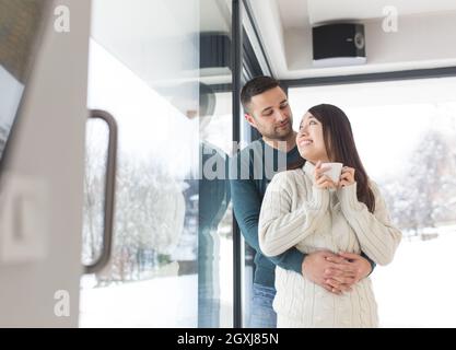 Glückliche junge Multiethnischen Paar beim Kaffee am Morgen durch das Fenster in der Kälte des Winters Tag zu Hause Stockfoto