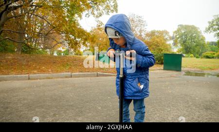 Porträt eines traurigen und verärgerten kleinen Jungen, der auf dem Roller im Park reitet. Stockfoto