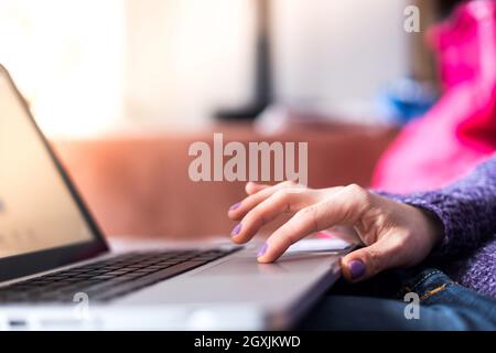 Mädchen mit violetten Fingernägeln benutzt ihren Laptop zu Hause auf der Couch Stockfoto