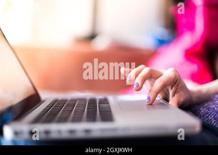 Mädchen mit violetten Fingernägeln benutzt ihren Laptop zu Hause auf der Couch Stockfoto