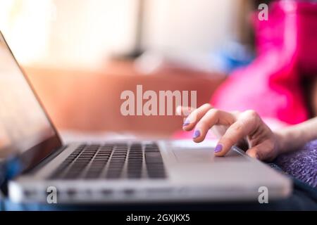 Mädchen mit violetten Fingernägeln benutzt ihren Laptop zu Hause auf der Couch Stockfoto