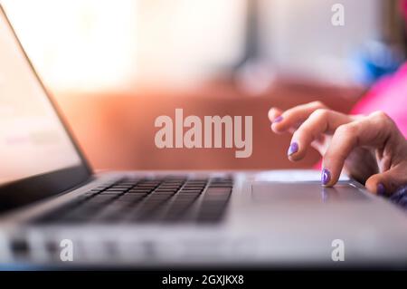 Mädchen mit violetten Fingernägeln benutzt ihren Laptop zu Hause auf der Couch Stockfoto