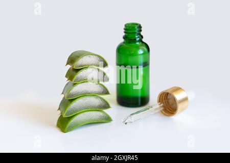 Eine kleine grüne Flasche mit einer Pipette und geschnittenen Aloe Vera verlässt die Blätter aus nächster Nähe Stockfoto