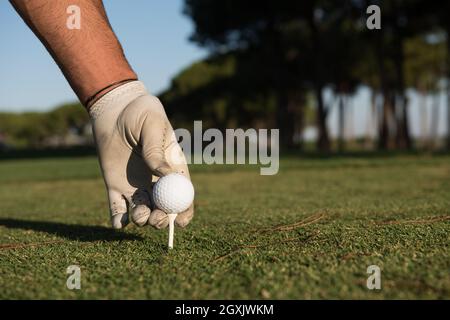 Nahaufnahme des Golf Spieler Hand Ball am Abschlag zu platzieren. Schöner Sonnenaufgang am Golfplatz Landschaft im Hintergrund Stockfoto