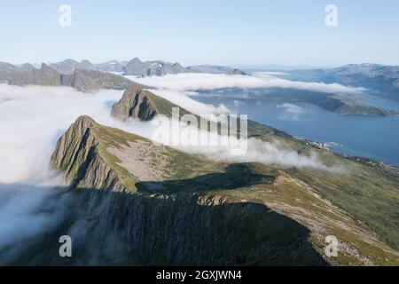 Luftaufnahme über wolkenbedeckte Bergkette am Mt. Husfjell, Blick Richtung Fjord Bergsfjord, Senja Insel, Norwegen Stockfoto