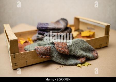 Konzept - der Herbst ist die Zeit zum Aufwärmen und Handarbeiten.Handgestrickte Socken in Herbstfarben in einer Holzkiste auf Herbstlaub gestapelt Stockfoto