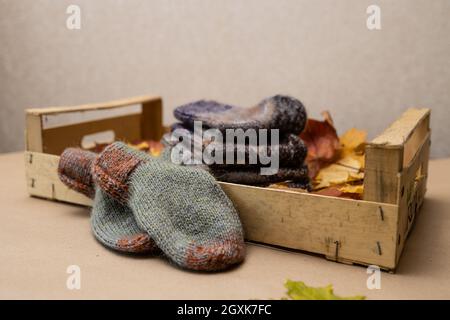Konzept - der Herbst ist die Zeit zum Aufwärmen und Handarbeiten.Handgestrickte Socken in Herbstfarben in einer Holzkiste auf Herbstlaub gestapelt Stockfoto