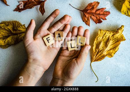 Hände mit Holzblöcken, die das Wort buchstabieren, fallen von Herbstblättern umgeben Stockfoto